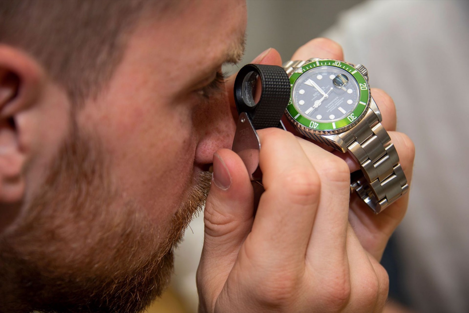 A member of staff inspecting a wristwatch through a jeweller's loupe